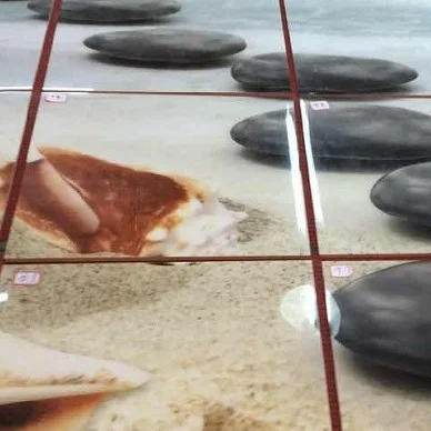 Ausschnitt eines 3D-Bodenmotivs mit dunklen Steinen auf Sand, Fliesenfugen und Nummerierung der Fliesen sichtbar