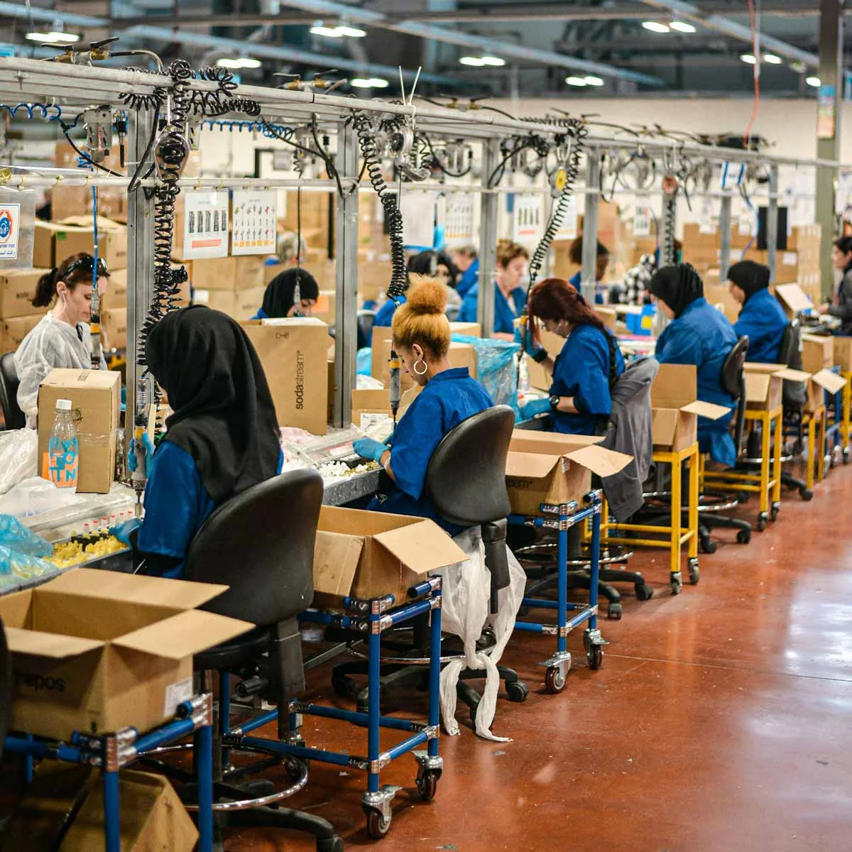 Mitarbeiterinnen und Mitarbeiter an einer Produktionslinie mit Kartons und Arbeitsplätzen